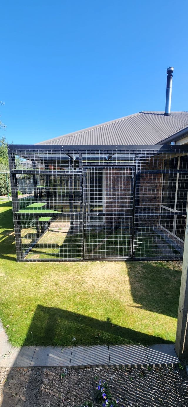 Black mesh catio running along a brick house under the roofline