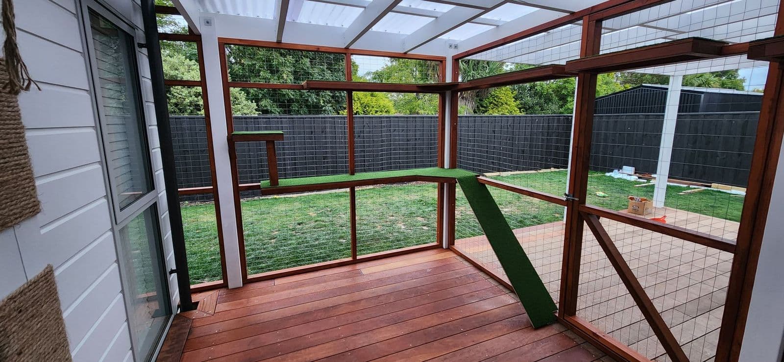 Catio built over a timber deck with turf ramp and shelves beside a sliding door