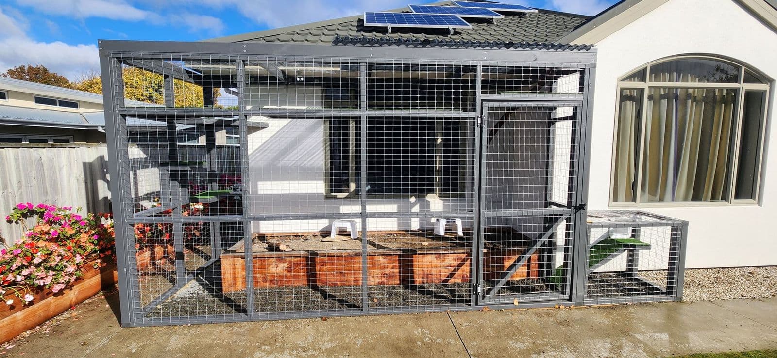 Charcoal-framed catio against a white house enclosing a raised garden bed